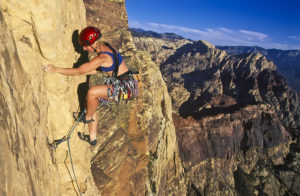 Female climber struggles up the edge of a challenging cliff.